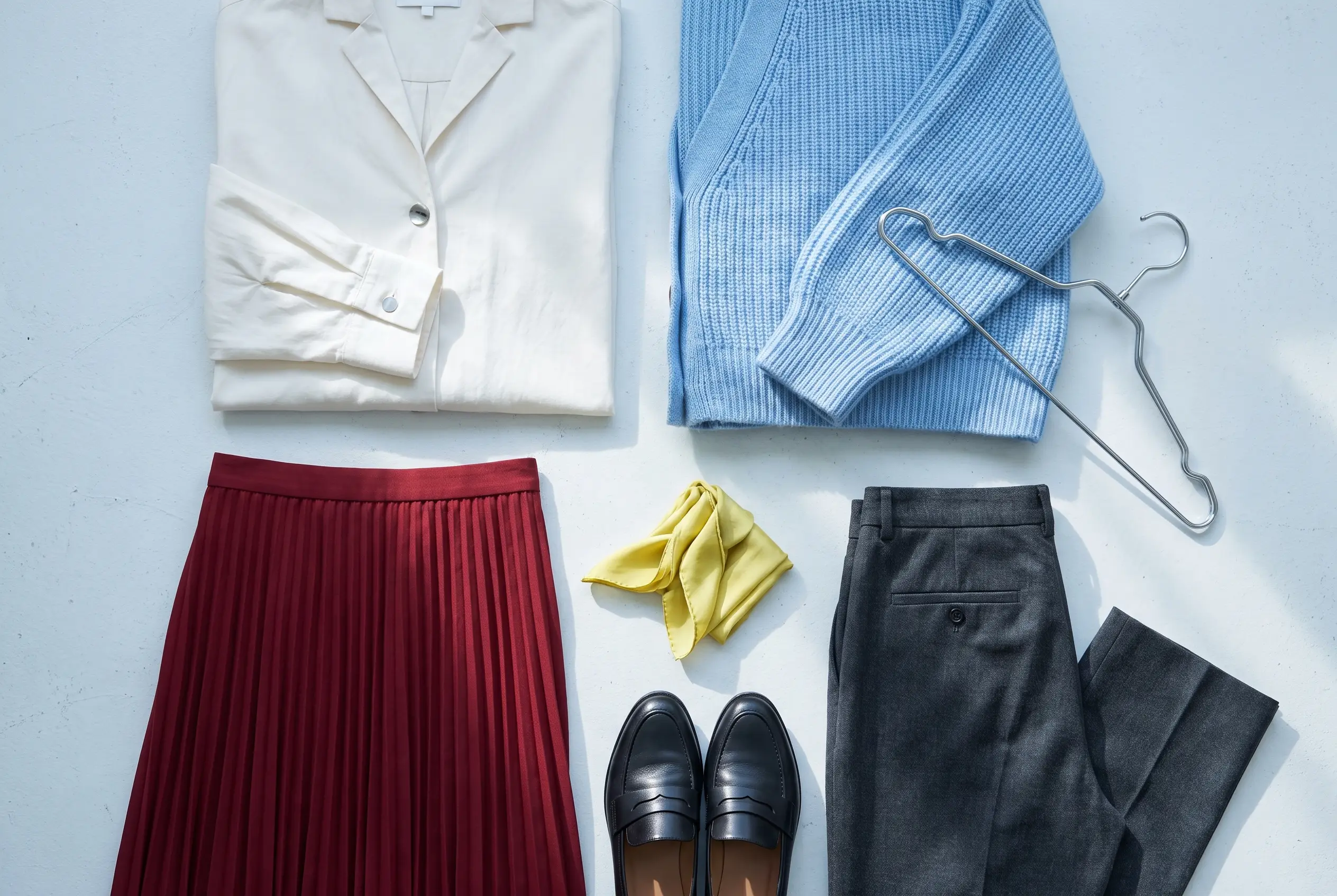 Blue knit, ivory shirt, pleated skirt, charcoal trousers and black loafers arranged together
